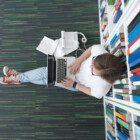 female student study in school library, using tablet and searching for information’s on internet. Listening music and lessons on white headphones