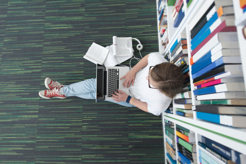 female student study in school library, using tablet and searching for information’s on internet. Listening music and lessons on white headphones