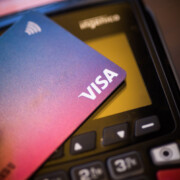 Bucharest, ROMANIA - May 17, 2021: Illustrative editorial concept image of a person holding a VISA card near a POS terminal.
