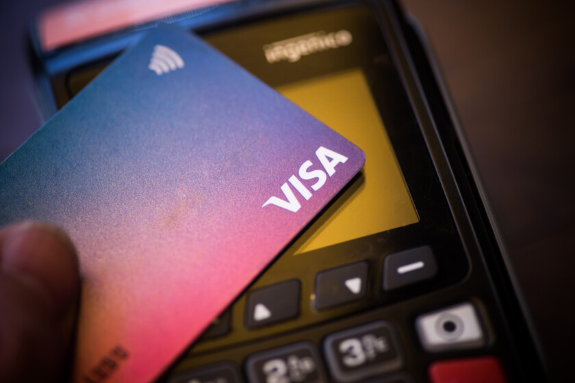 Bucharest, ROMANIA - May 17, 2021: Illustrative editorial concept image of a person holding a VISA card near a POS terminal.